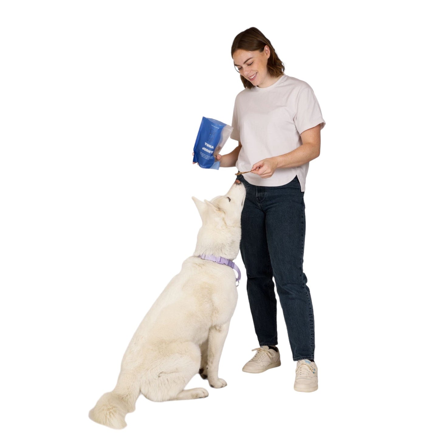 Woman holding a blue container interacting with a white dog on a white background