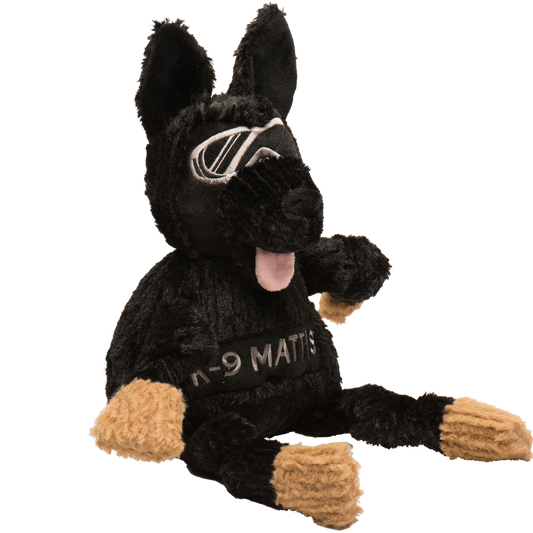 Black plush K-9 Mattis toy with tan paws, embroidered goggles, pink tongue, and "K-9 MATTIS" on its chest.