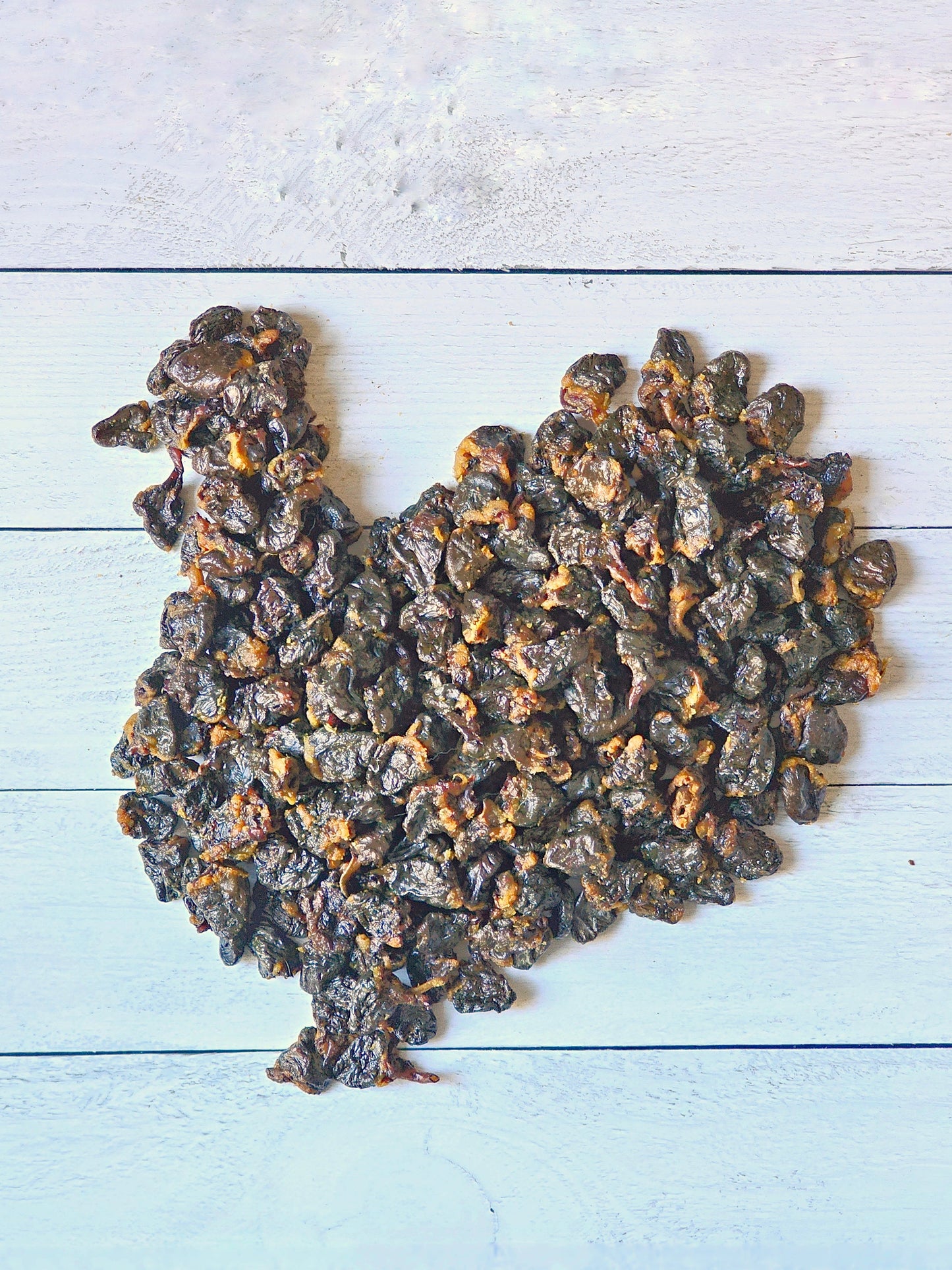 Dark brown sliced turkey heart dog treats by Naked Beasts arranged in a turkey shape on white wood planks.