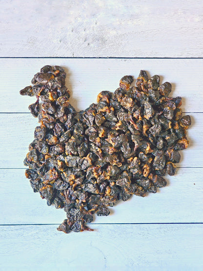 Dark brown sliced turkey heart dog treats by Naked Beasts arranged in a turkey shape on white wood planks.