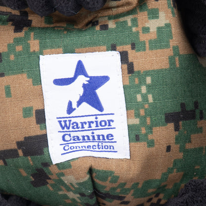 Close-up of Luke Black Lab plush toy with camo fabric and a white Warrior Canine Connection tag with blue logo.