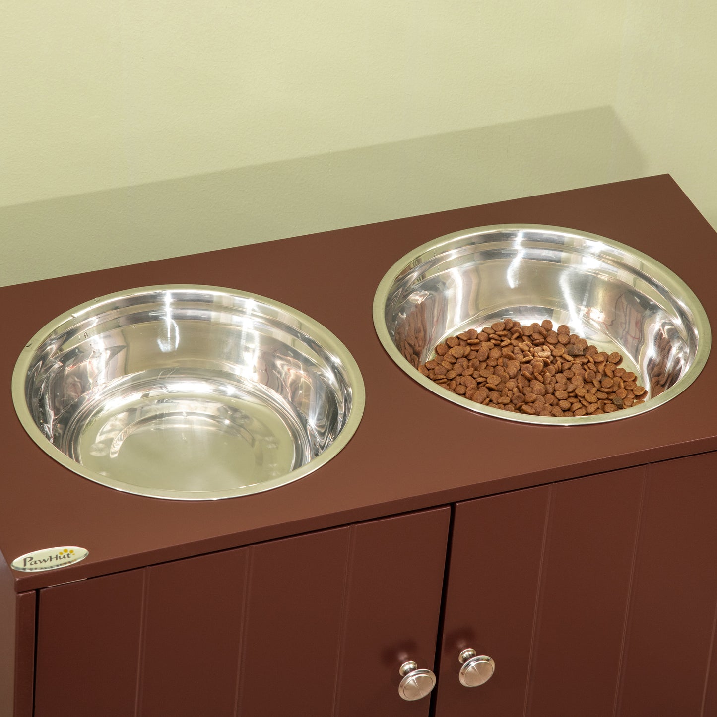 Elevated brown wood dog feeder cabinet with two stainless steel bowls and a storage compartment with silver knobs.