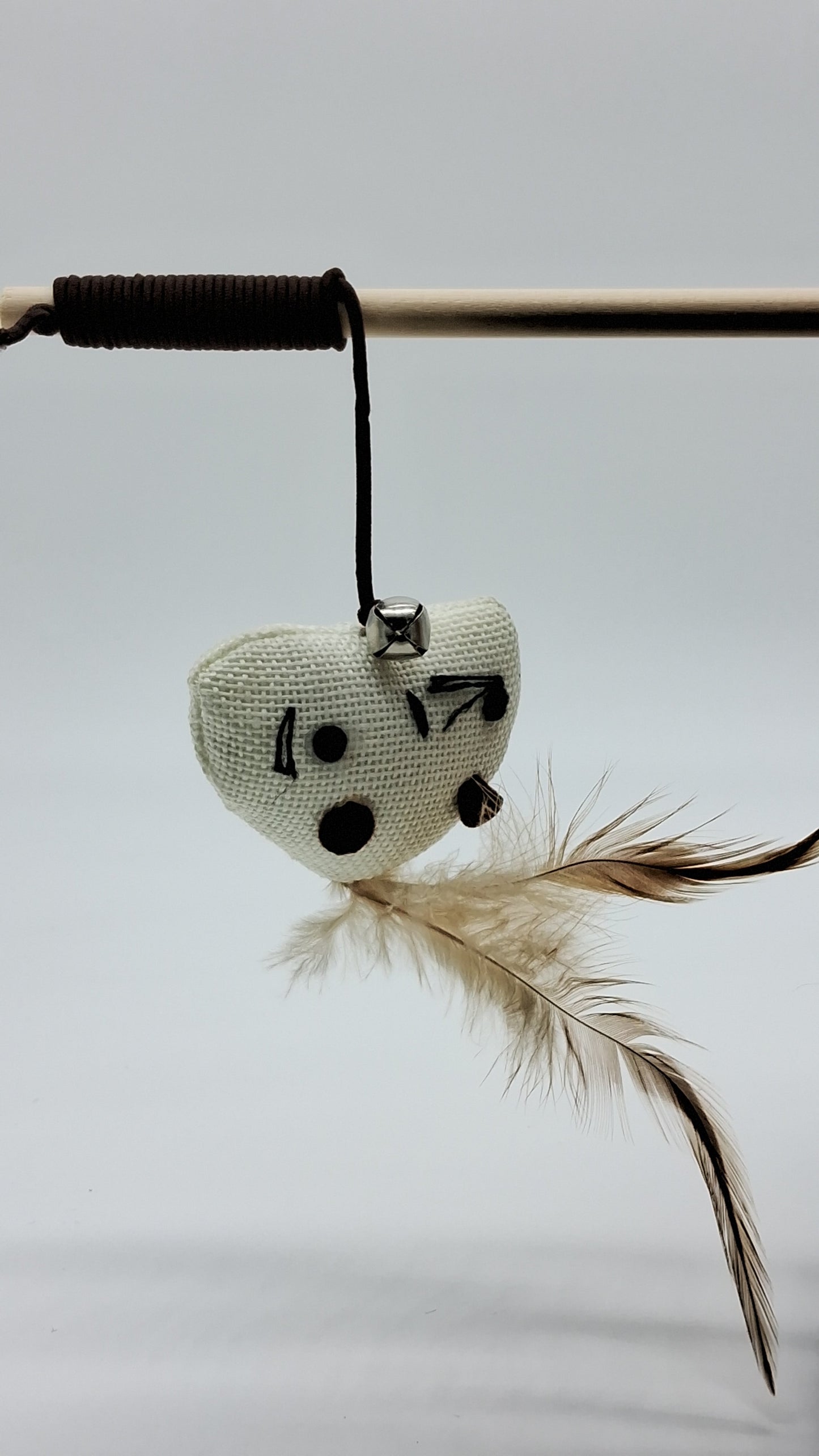 Toys N Treats Box cat teaser wand with a wooden rod, white heart plush, silver bell, and natural brown feathers.