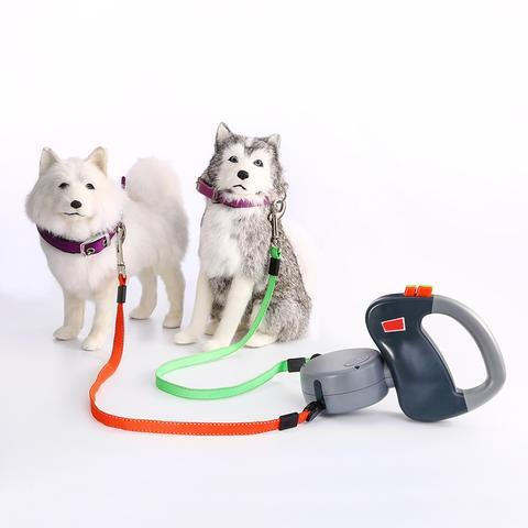 Estely dual retractable dog leash with a grey handle and orange and green straps, shown with two stuffed dogs.