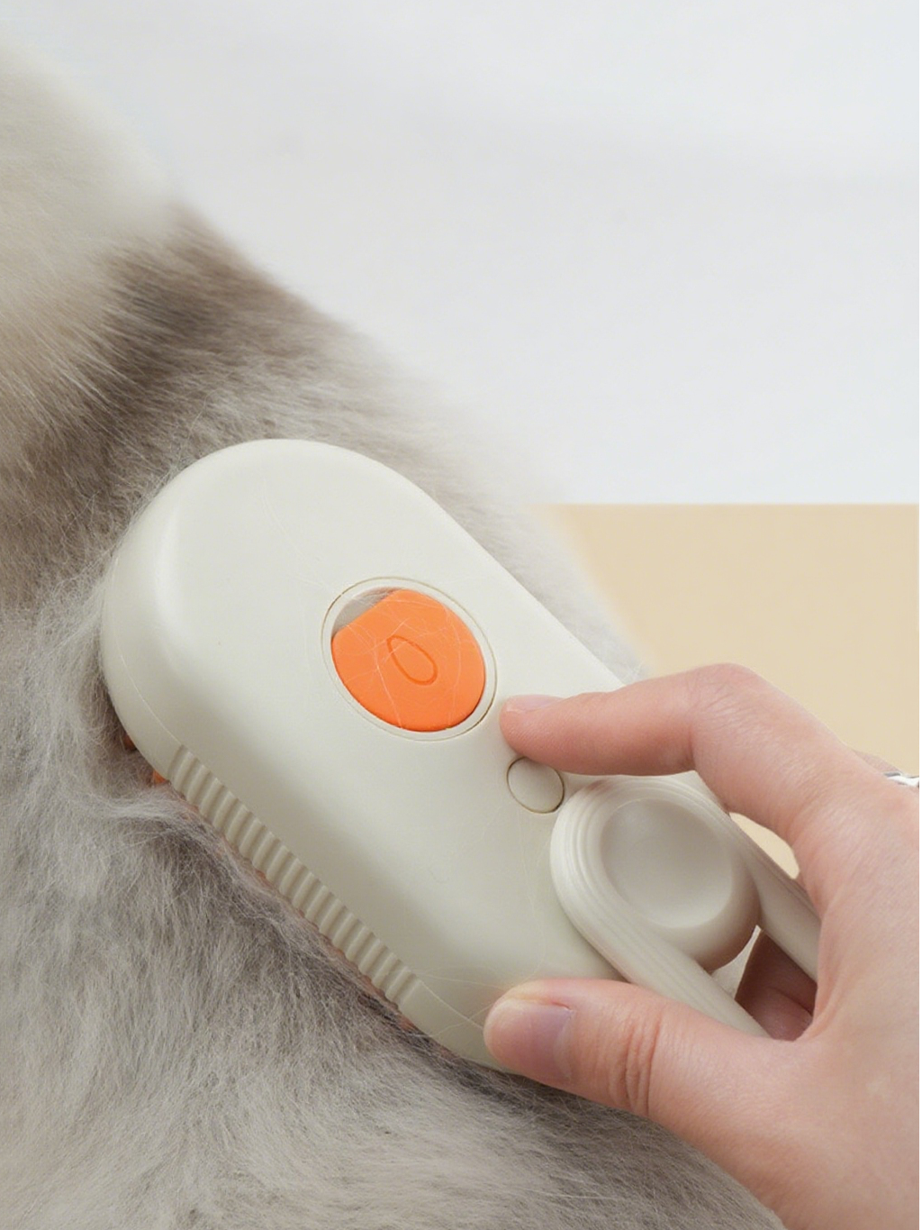 Purrfect Pet Kingdom cream steam brush with orange button deshedding a long-haired cat's soft grey fur.