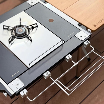 Black and silver metal Snow Peak camping stove featuring a gas burner, side racks, and a bamboo wood table extension.