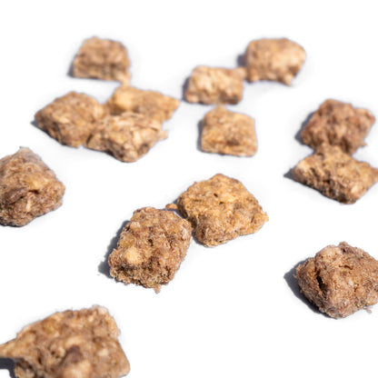 Bite-sized tan and brown freeze-dried chicken crisp dog treats by Wasatch Pup scattered on a white background.