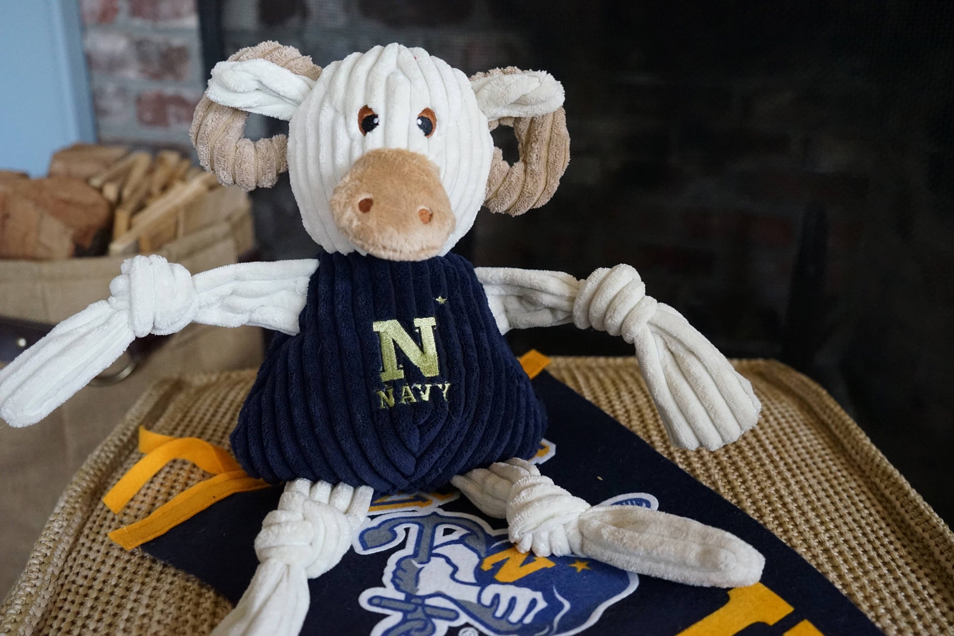 Plush corduroy Navy goat dog toy with knotted limbs, sitting on a matching team pennant.