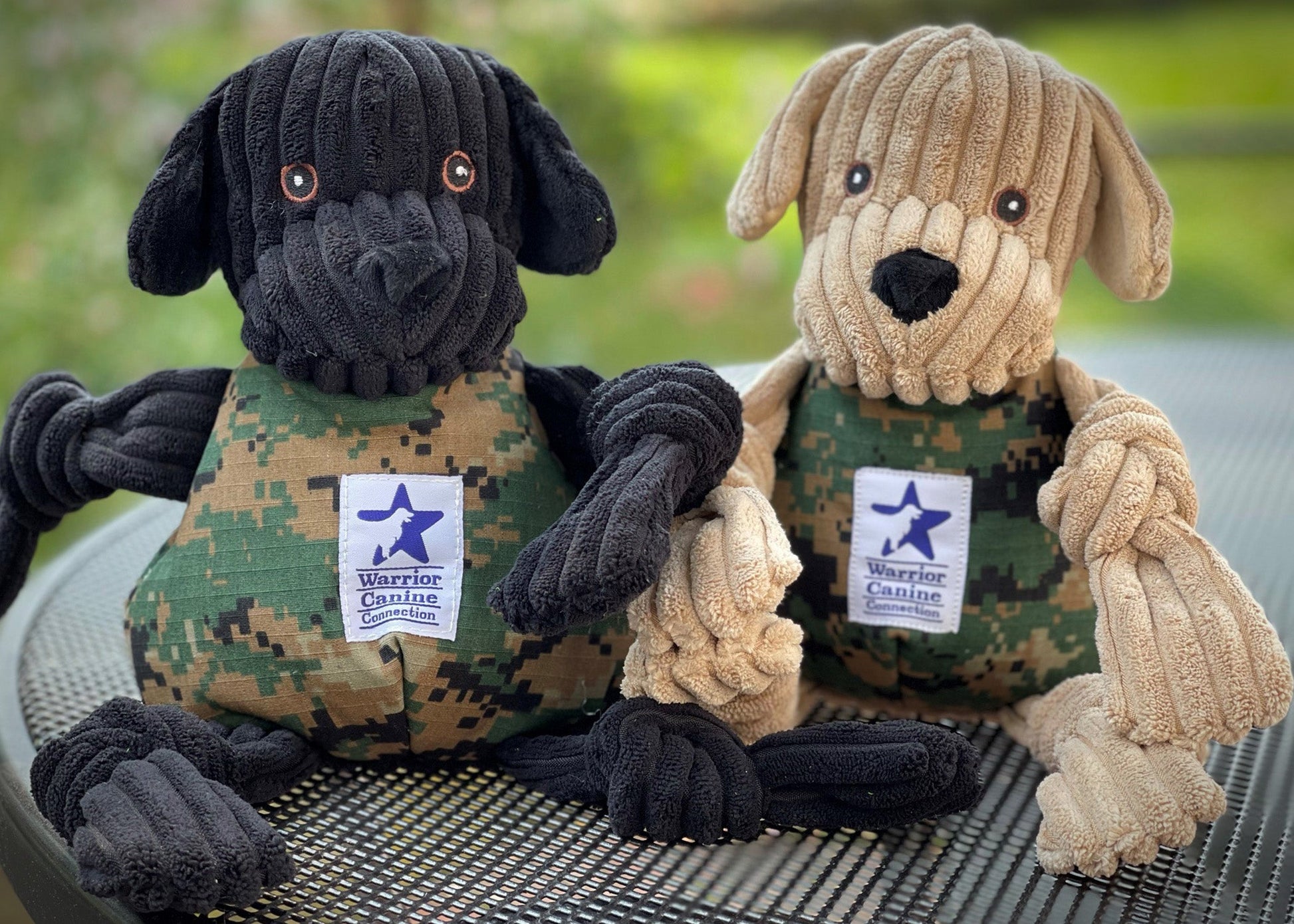 Black and tan corduroy plush dog toys in camo vests with Warrior Canine Connection patches and knotted limbs.