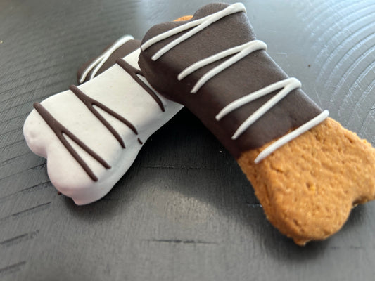 Lucy Loo Peanut Butter and Pumpkin bone treats with dark and white icing drizzles on a dark surface.