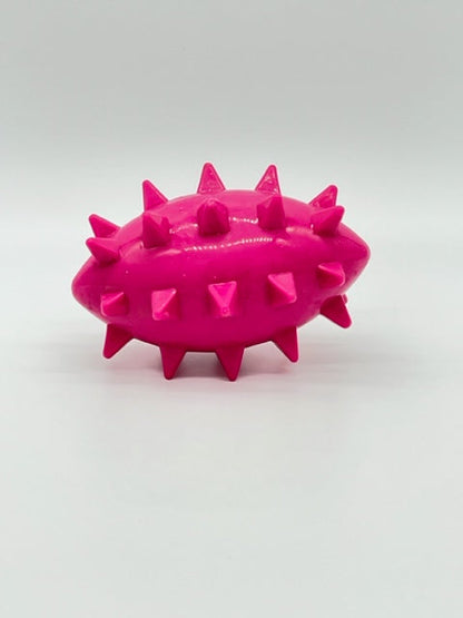 Bright pink, football-shaped rubber dog toy with large spikes. Spikez the Ball by Toys N Treats Box.