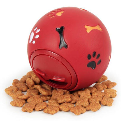 Red interactive dog enrichment puzzle feeder ball with paw and bone designs surrounded by dog treats