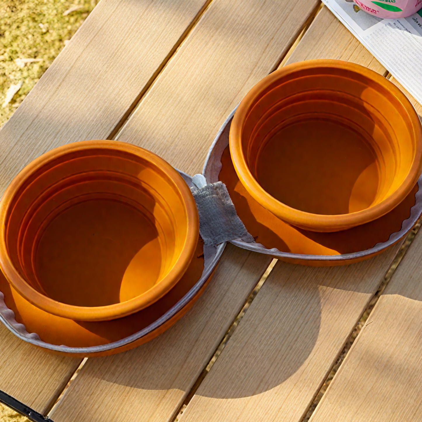 Two orange foldable pet travel bowls stacked together, set on a wooden table for outdoor use