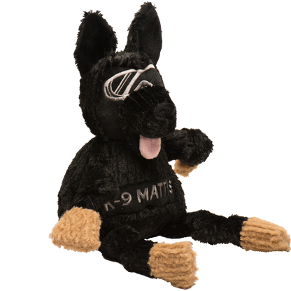 Black plush K-9 Mattis toy with tan paws, embroidered goggles, pink tongue, and "K-9 MATTIS" on its chest.