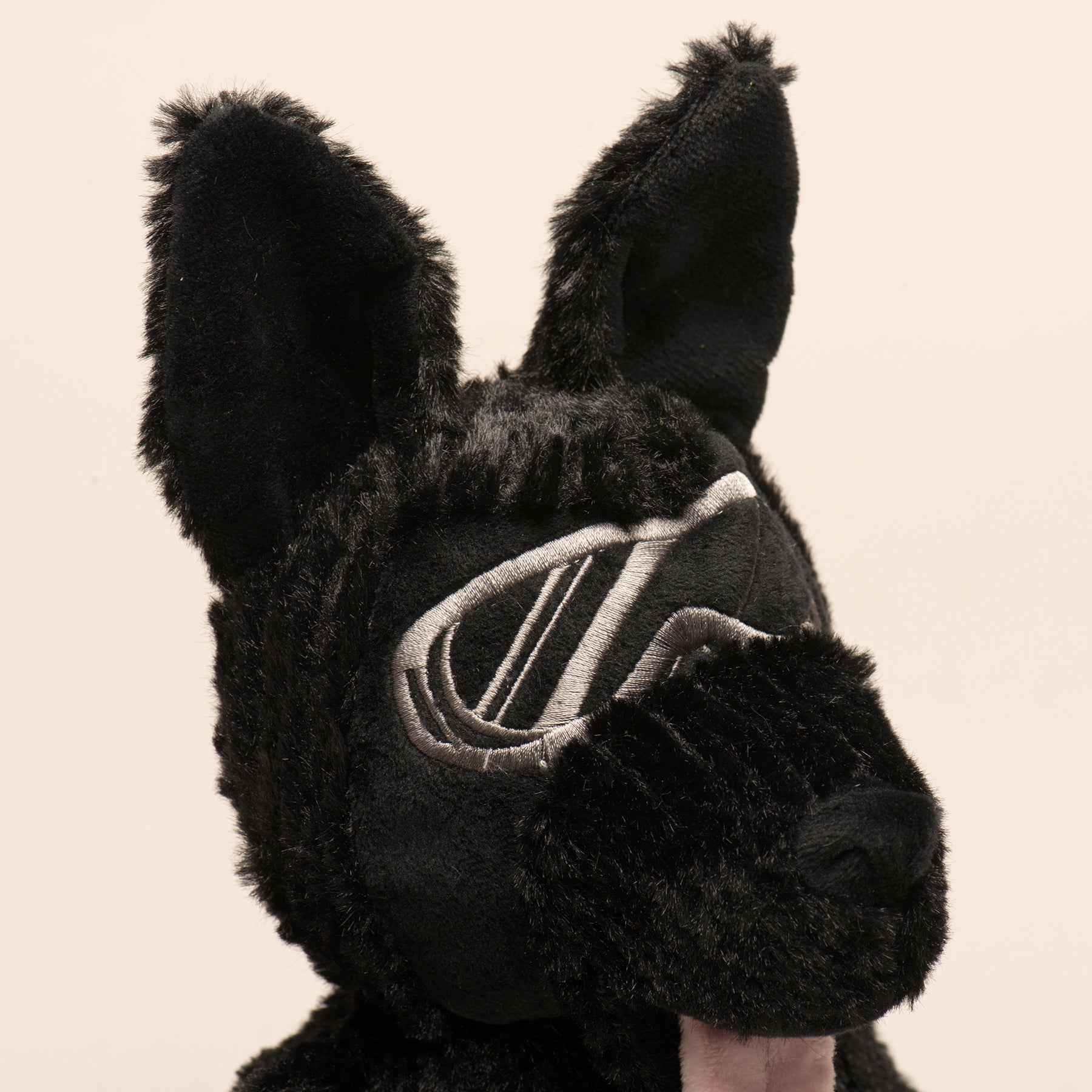 Close-up of a black fuzzy plush dog toy with pointy ears and embroidered silver goggles. Mattis Hero interactive toy.