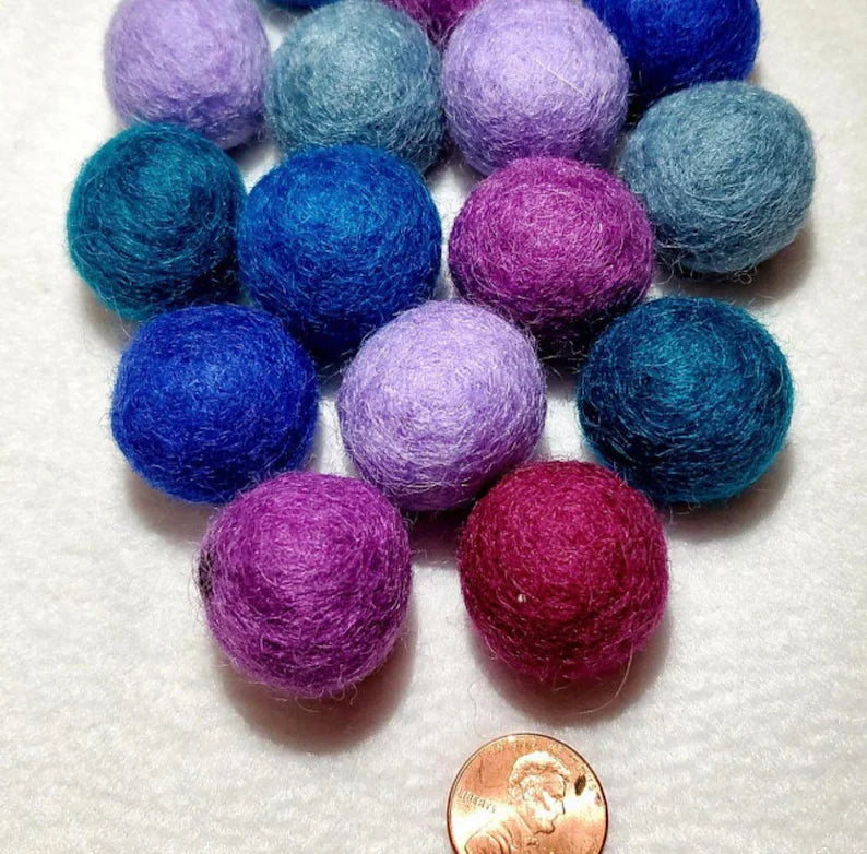 Blue and purple organic wool cat ball toys by ReNewedPet. Small, fuzzy felted balls shown with a penny for scale.