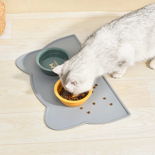 Gray non-slip dog bowl placemat with cat eating from bowls on a wooden floor