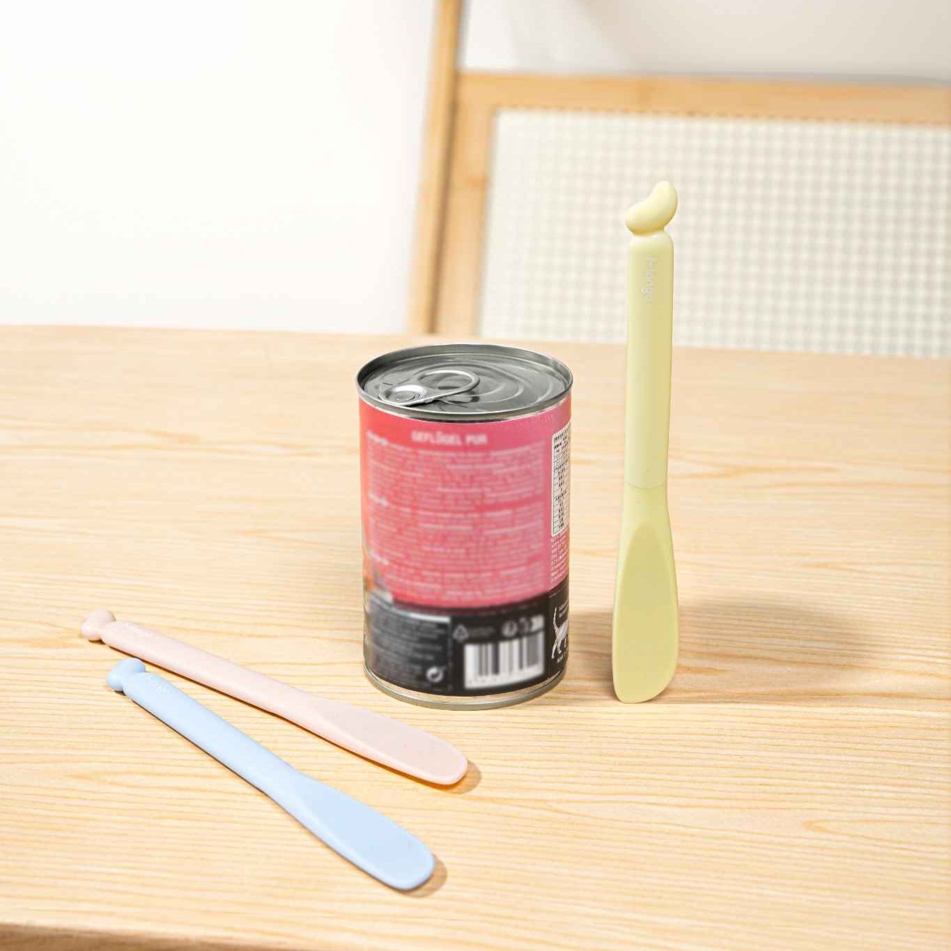 MangoPets pet food can spoon in pastel colors next to a can of pet food on a wooden table