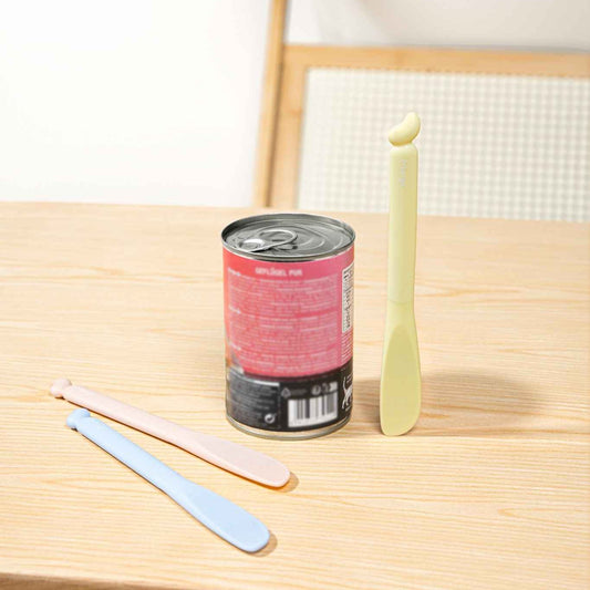 MangoPets pet food can spoon in pastel colors next to a can of pet food on a wooden table