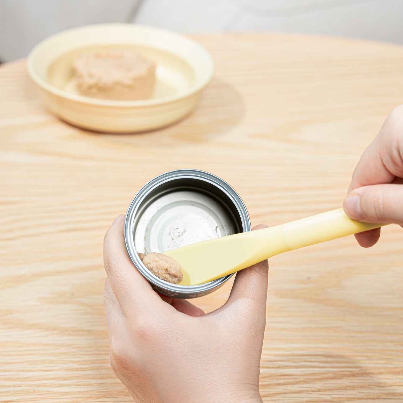 Person using a pet food can spoon to scoop food from a can into a bowl