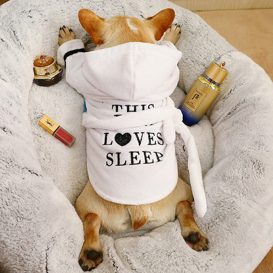 Cute dog in a cozy dog hooded bathrobe that says This Loves Sleep, resting on a soft pet bed