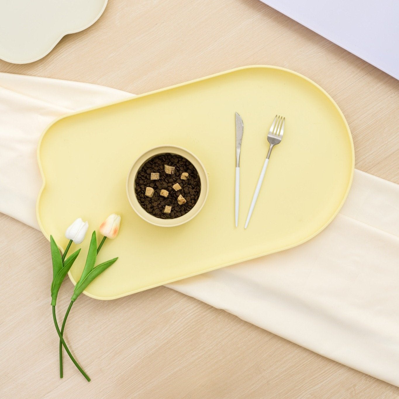 MangoPets waterproof pet feeding mat in soft yellow with a bowl and utensils for pets