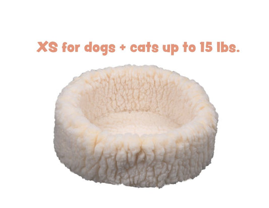 Cream HuggleFleece round pet bed with thick walls. Text: XS for dogs + cats up to 15 lbs.